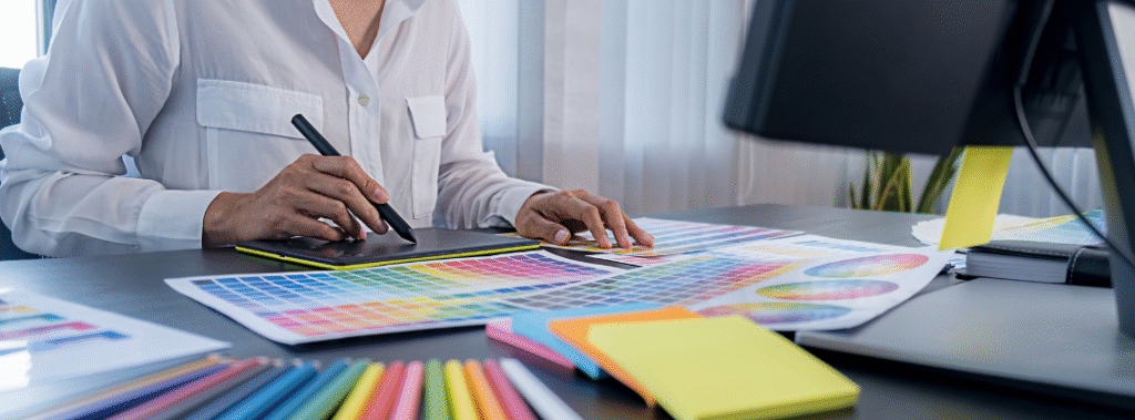Designer using a pen tablet with color swatches on the desk, a clear case to hire a graphic designer when DIY design burnout hits