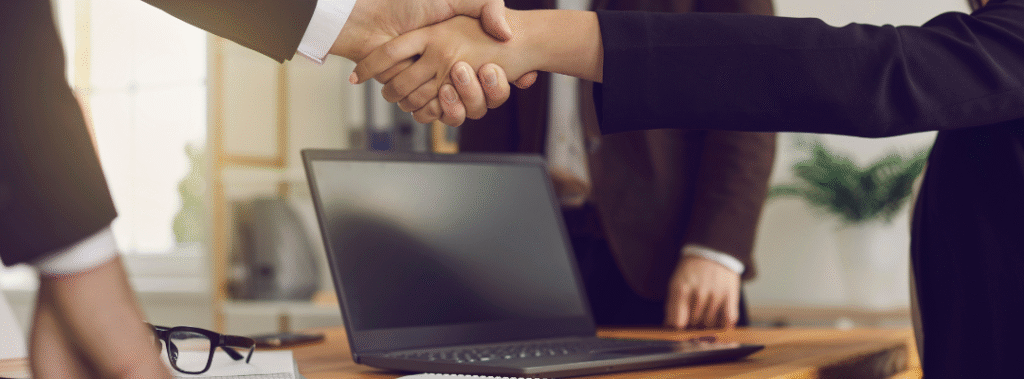 Business partners shaking hands in front of a laptop, symbolizing trust built through professional website design.