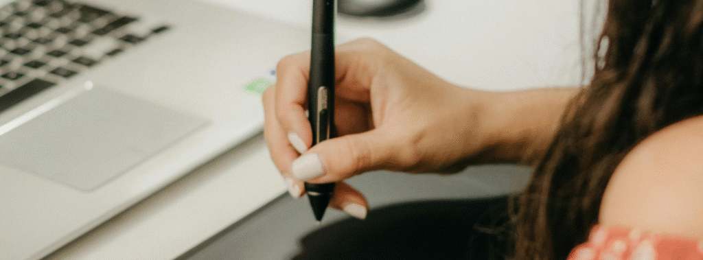 Hand holding a stylus over a tablet next to a laptop, a practical example of quick design tips for business.