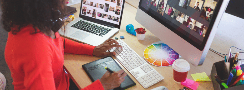 Designer updating a monthly graphic design maintenance plan checklist on a laptop, with social templates and print samples on the desk.
