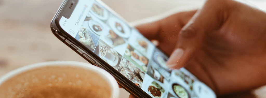Hand scrolling an Instagram grid on a smartphone beside a coffee cup, example for instagram carousel design tips.